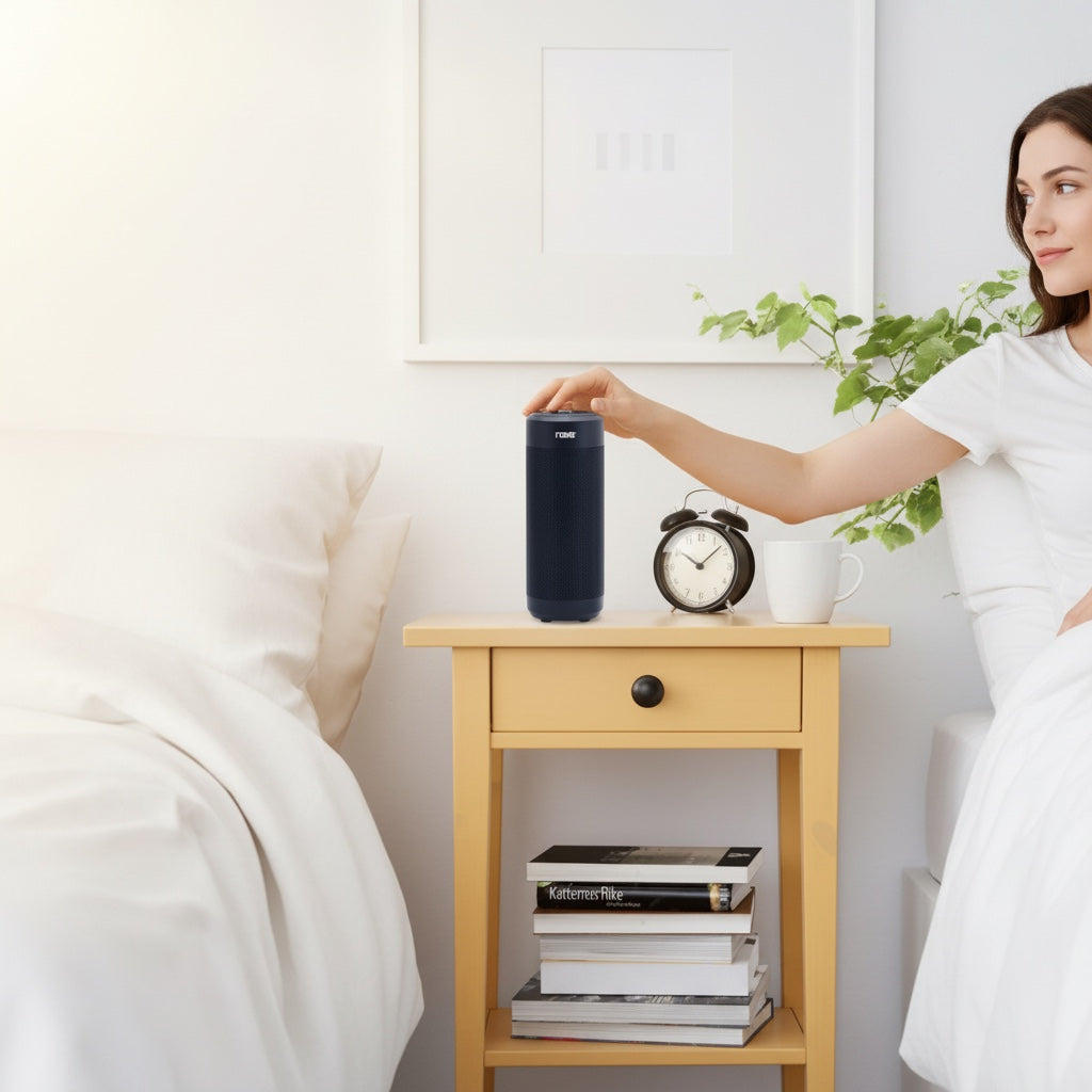 Hostecno Naxa wireless smart speaker in black, cylindrical design, placed on a nightstand next to a bed. Features voice control and Bluetooth connectivity.
